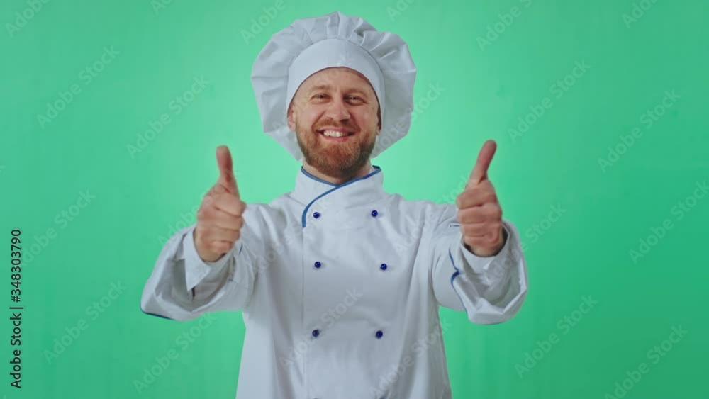 Very attractive baker man in the uniform green background showing a big like in front of the camera and smiling large Very attractive baker man in the uniform green background showing a big like in front of the camera and smiling large