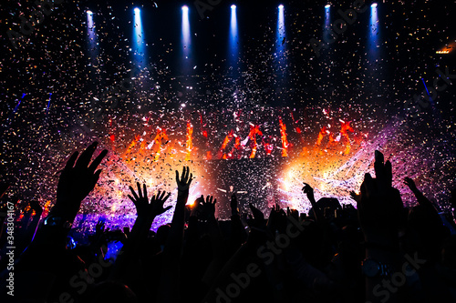 Fans hands raised up during the show. Bright lights and shiny confetti at a pop concert. happy youth dancing at a festival in a crowd. view of the stage.