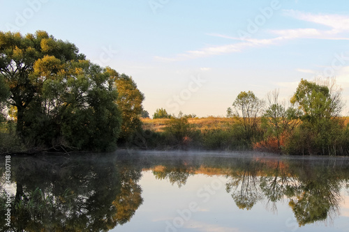 Morning rural scene. Little pond during sunrise. Trees reflects in clear water. Blue sky. Beautiful landscape.