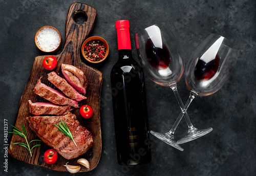 grilled beef steak with spices on a cutting board and a bottle of red wine, glasses on a stone background