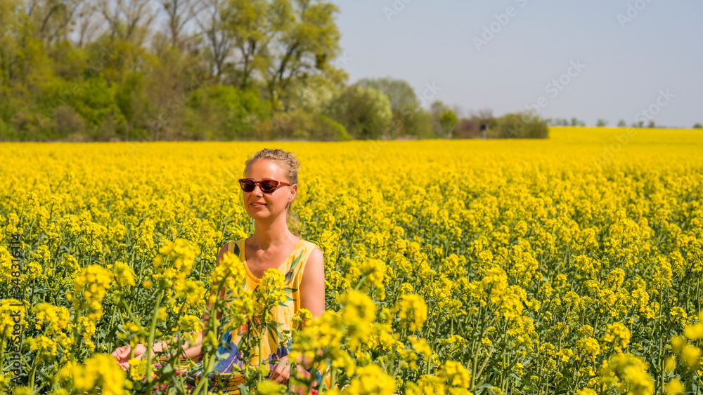 eine junge Frau sitzt in einem Rapsfeld in der Sonne