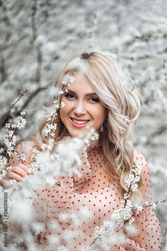 Woman with gorgeous smile, curly blond hair in red dress having fun in blooming garden Woman with gorgeous smile, curly blond hair in red dress having fun in blooming garden