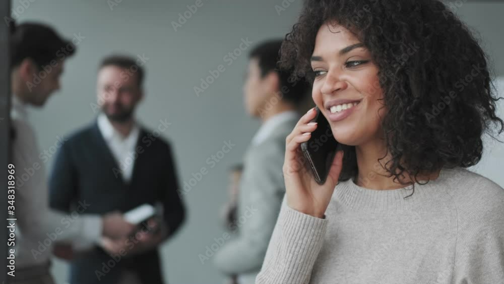 Amazing cheerful african young business woman indoors in office talking by mobile phone Amazing cheerful african young business woman indoors in office talking by mobile phone