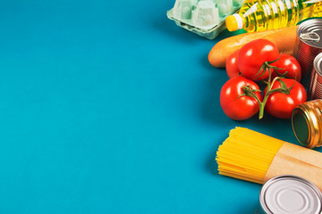 Food donations on green background with copyspace - pasta, fresh vegatables, canned food, baguette, eggs. Donation or delivery food concept