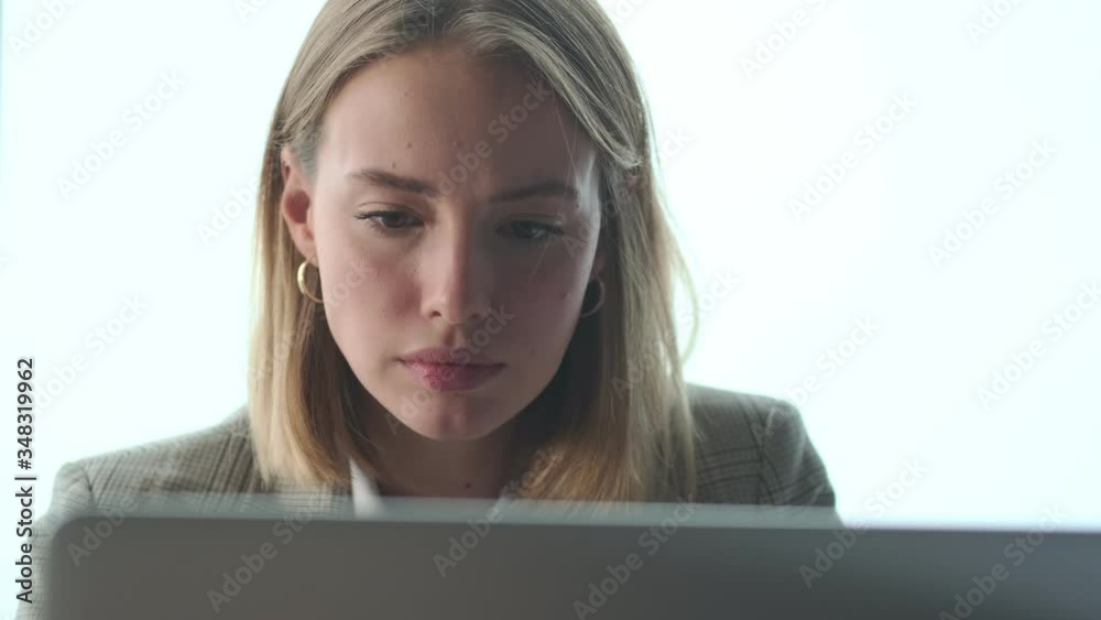 Pretty concentrated blonde young business woman indoors in office using laptop computer Pretty concentrated blonde young business woman indoors in office using laptop computer