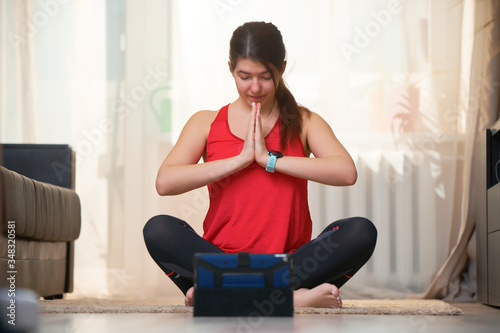 Woman practices yoga and meditates in the lotus position at home using video tutorials.