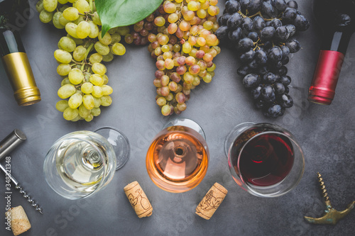 Glasses with white, red and pink wine and ripe grapes on black stone background, top view