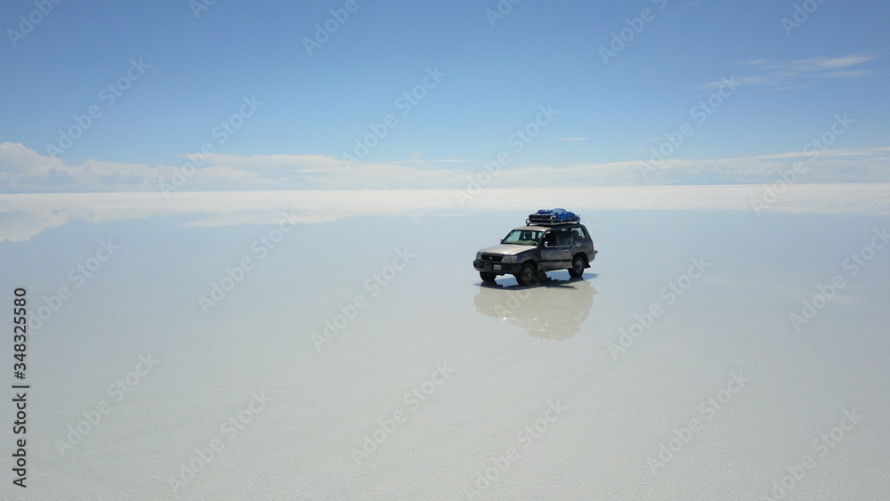 Car in Salar de Uyuni, Salt desert in Bolivia, seen with drone and Andes in the background