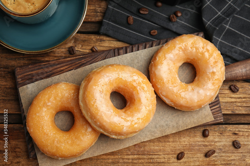 Delicious glazed donuts on wooden table, flat lay
