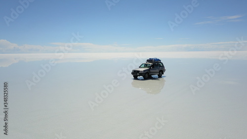 Car in Salar de Uyuni, Salt desert in Bolivia, seen with drone and Andes in the background