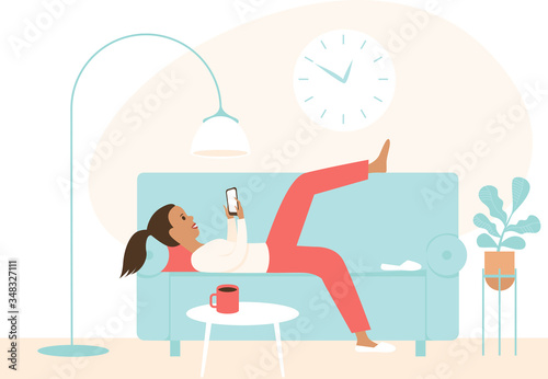 Lazy girl lying on a sofa using smartphone. Chatting in social media, procrastination. Concept for coronavirus COVID-19 quarantine self isolation