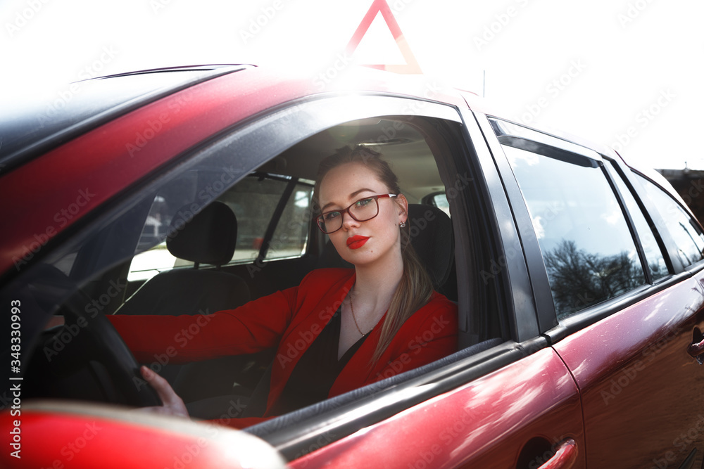 Young beautiful happy woman in red sitting at the wheel new training car.