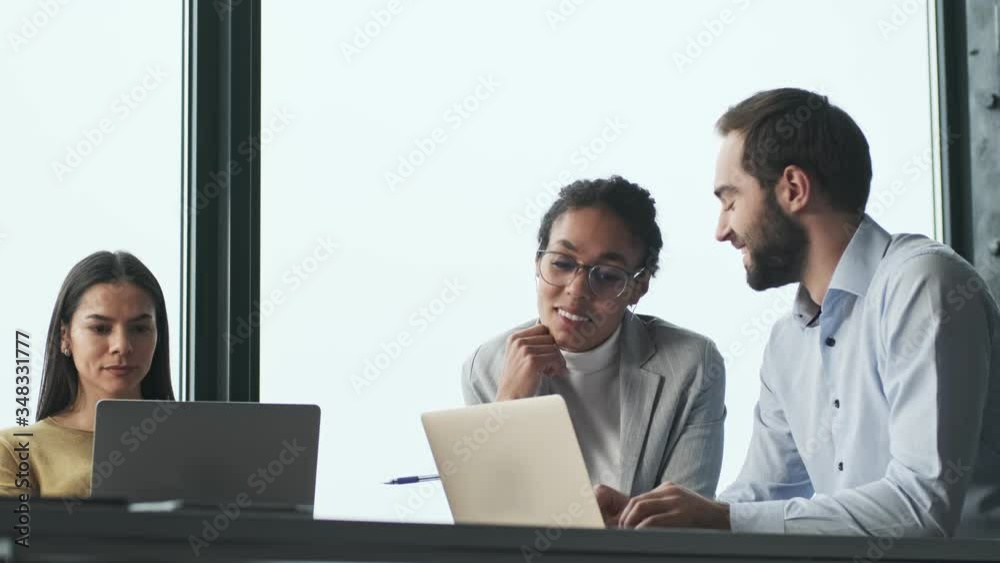 Young smiling colleagues talking with each other in office work with laptop Young smiling colleagues talking with each other in office work with laptop