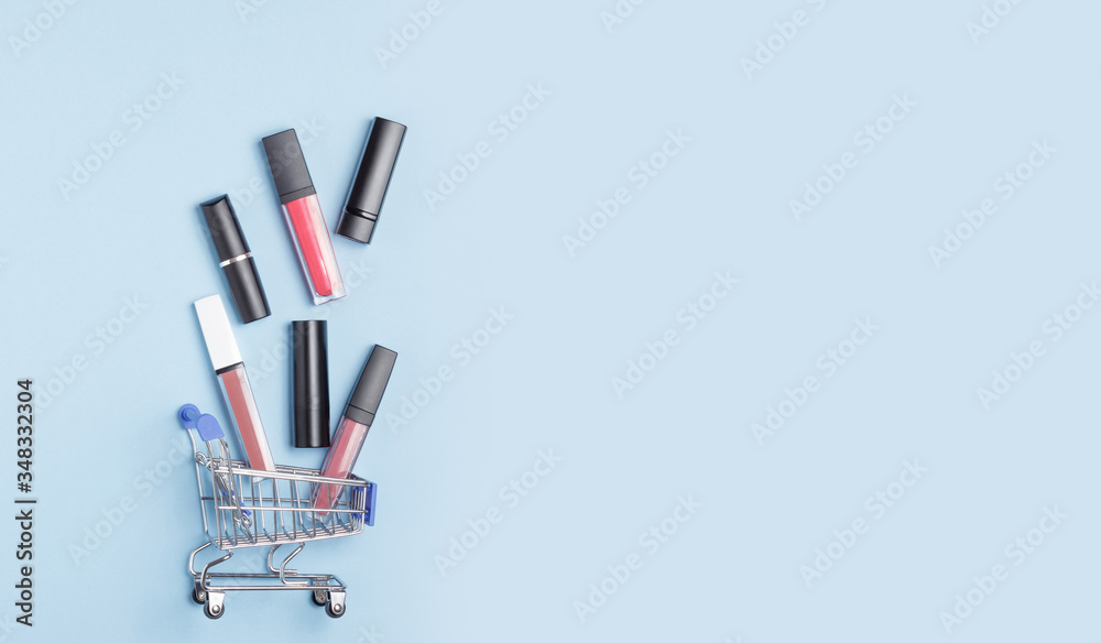 Women's lipsticks and lip glosses in a shopping trolley on a blue background. The concept of buying cosmetics, online shopping. Women's lipsticks and lip glosses in a shopping trolley on a blue background. The concept of buying cosmetics, online shopping.