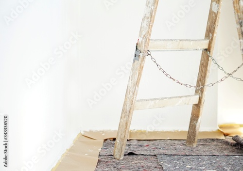 Real old wooden ladder of a painter in use for an interior renovation. Painter cover fleece for protection of floor surfaces. stepladder with chains and paint splashes.
