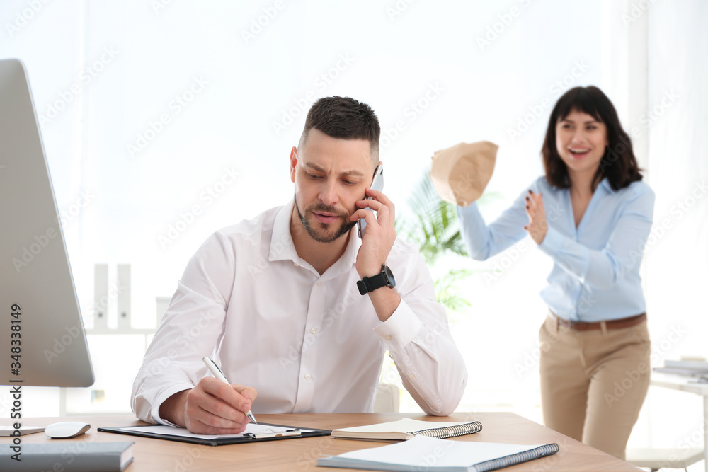 Young woman popping paper bag behind her colleague in office. April fool's day Young woman popping paper bag behind her colleague in office. April fool's day