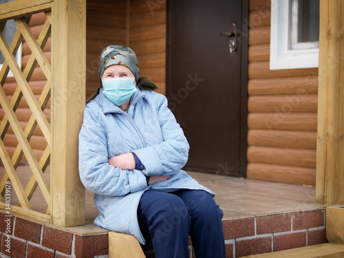 an elderly woman wears a medical face mask and recovers from an illness near her home during the quarantine and the Crown Virus pandemic.