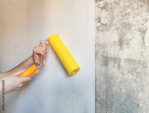 Tool, roller for smoothing wallpaper yellow. Paint roller with a red handle and a yellow smooth nozzle on a light background. Wallpapering in the apartment.