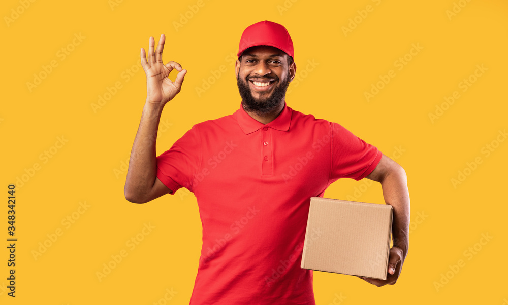 Courier Guy Holding Cardboard Box Gesturing Okay On Yellow Background Courier Guy Holding Cardboard Box Gesturing Okay On Yellow Background
