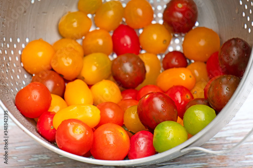 A mix of sweet cherry and grape tomatoes in a colander, washed and ready to be eaten. Focus on the first row of tomatoes.