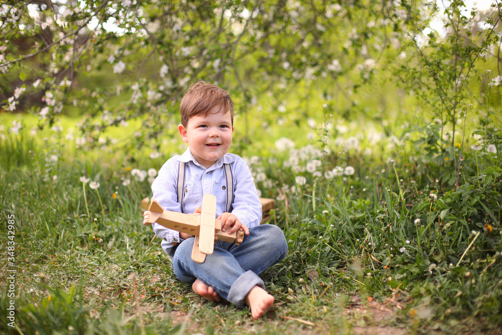 Little cute blond boy playing with a wooden plane in the summer park on the grass on a sunny day Little cute blond boy playing with a wooden plane in the summer park on the grass on a sunny day