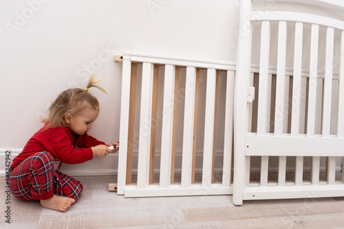 Little child tries to assemble children bed with screwdriver in white room with white walls.Copy space.