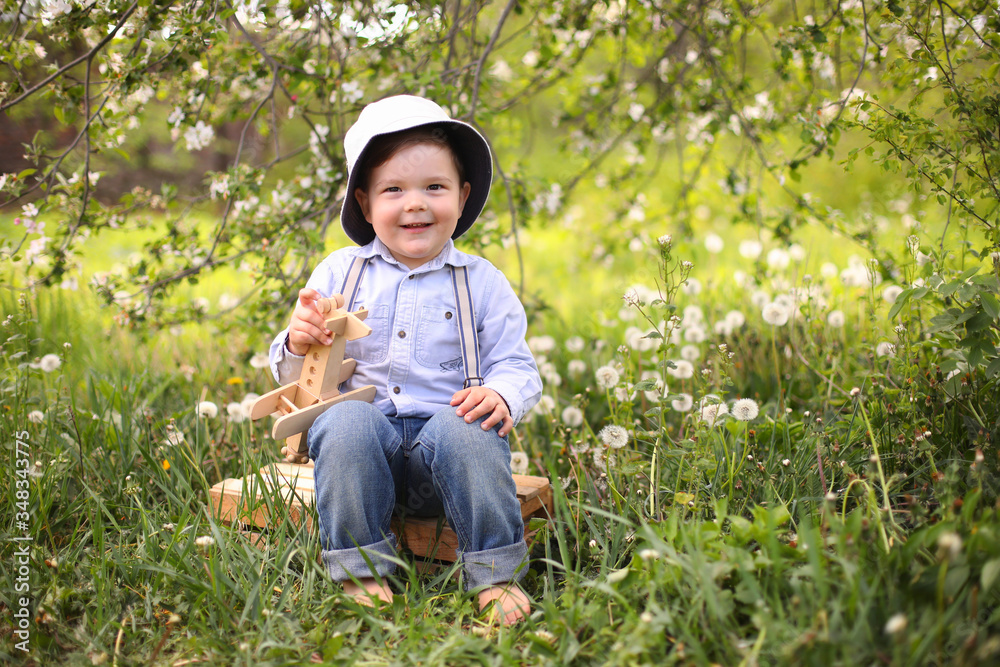 Little cute blond boy playing with a wooden plane in the summer park on the grass on a sunny day Little cute blond boy playing with a wooden plane in the summer park on the grass on a sunny day