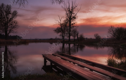 Old wooden pier on the lake against the background of a beautiful sunset in the cloudy sky. Beautiful landscape.