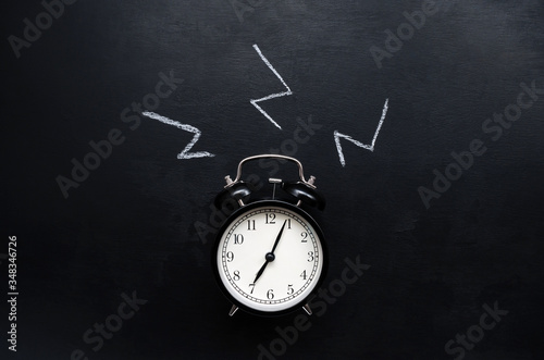 a black alarm clock with a white dial shows the time of 7 hours and rings on a black slate background with place for text