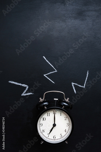 drawn sound. a black alarm clock with a white dial shows the time of 7 hours and rings on a black slate background with place for text