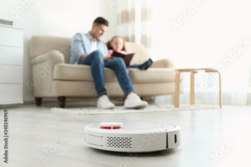 Man and his daughter resting while robotic vacuum cleaner doing its work at home