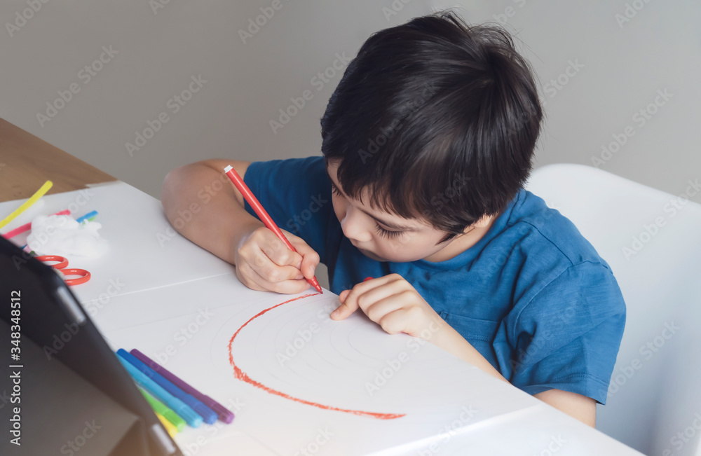 Kid red pen colouring rainbow on paper,Child using digital tablet for homework online lesson,Boy enjoy art activity at home, self-isolation, online education, home schooling, distance learning concept Kid red pen colouring rainbow on paper,Child using digital tablet for homework online lesson,Boy enjoy art activity at home, self-isolation, online education, home schooling, distance learning concept