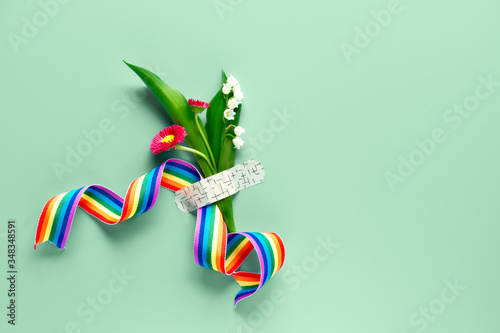 Thank you doctors and nurses! Rainbow ribbon in hand of mature woman with chamomile flower and grass bouquet attached with medical aid patch. Creative flat lay. Mint green background, copy-space. photo