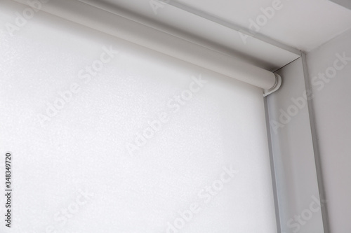 white rolled textile blinds on the window in a room, object of protection against sunlight close up with copy space.