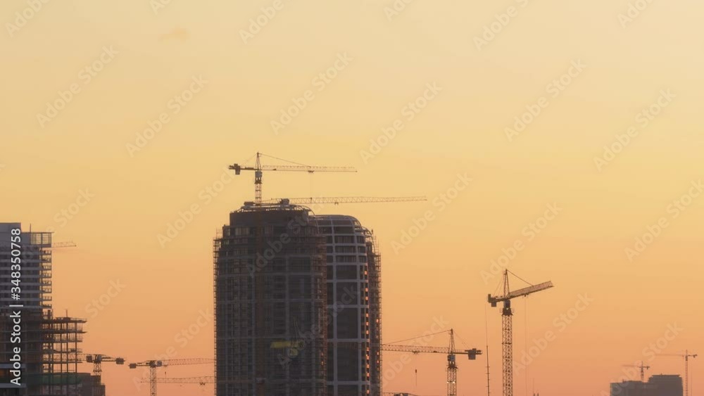 Aerial shot of the skyscraper building site in the process of construction in 4K VIDEO. In the background working cranes, flaying birds and sunset sky. Aerial shot of the skyscraper building site in the process of construction in 4K VIDEO. In the background working cranes, flaying birds and sunset sky.