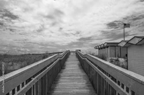Outdoor wooden boardwalk walkway, with sky and cloud background. Beach cabana pier plank bridge.