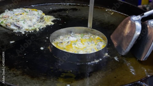 Appetizing sizzling oyster omelette ( Hoy Tod ) being cooked on a hot pan - delicious street food in Thailand