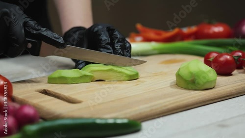 Hands in black gloves slicing avocado on wooden board