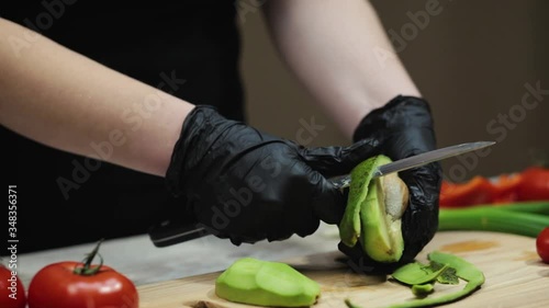 Female chef peels off avocado with a sharp knife at the wooden cutting board at the kitchen