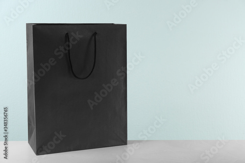 Black shopping paper bag on table against light background. Space for text