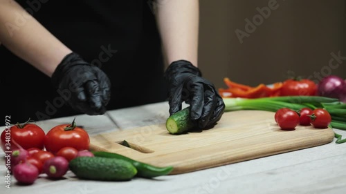 Female chef cuts cucumber with a sharp knife at the wooden cutting board at the kitchen