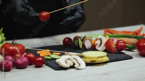 Woman hands in black gloves puts vegetables on wooden sticks for grill. Close up