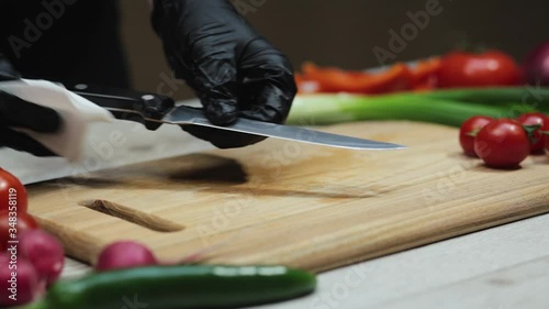 Woman in black gloves clean knife after finish of preparing food at the kitchen