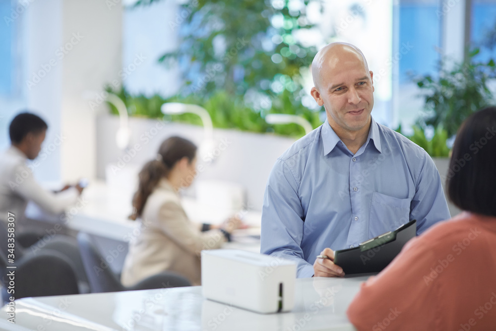 Portrait of mature manager smiling at client or customer while standing at reception desk, copy space Portrait of mature manager smiling at client or customer while standing at reception desk, copy space