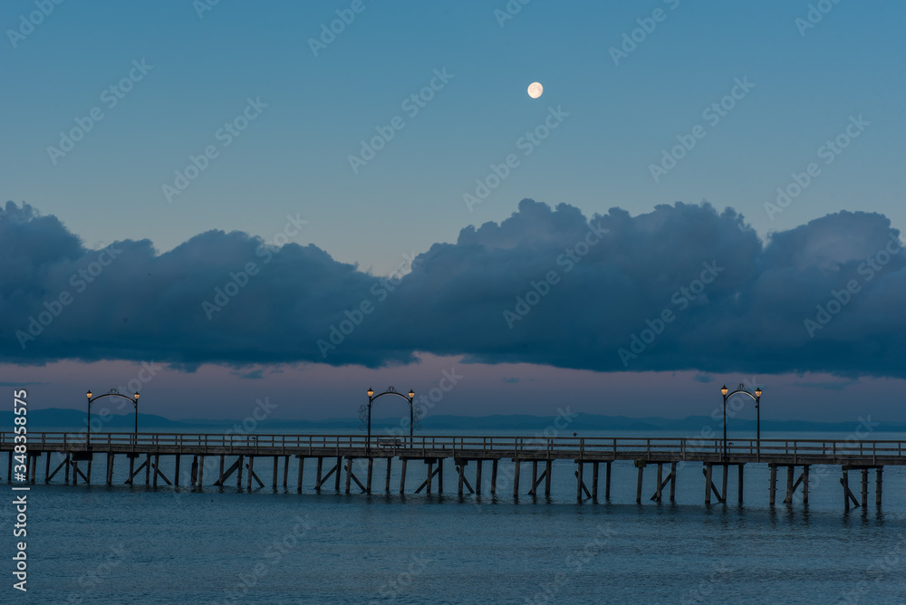 The moon sets over a pier on the West Coast of Canada
