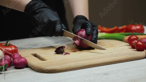Woman in black gloves slicing red onion on wooden cutting board in the kitchen