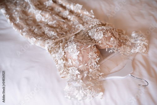 outfit of the bride ,the wedding dress lies on the bed, white bedding, the bride?s room, the morning before the wedding, the dress is decorated with fabric flowers,
