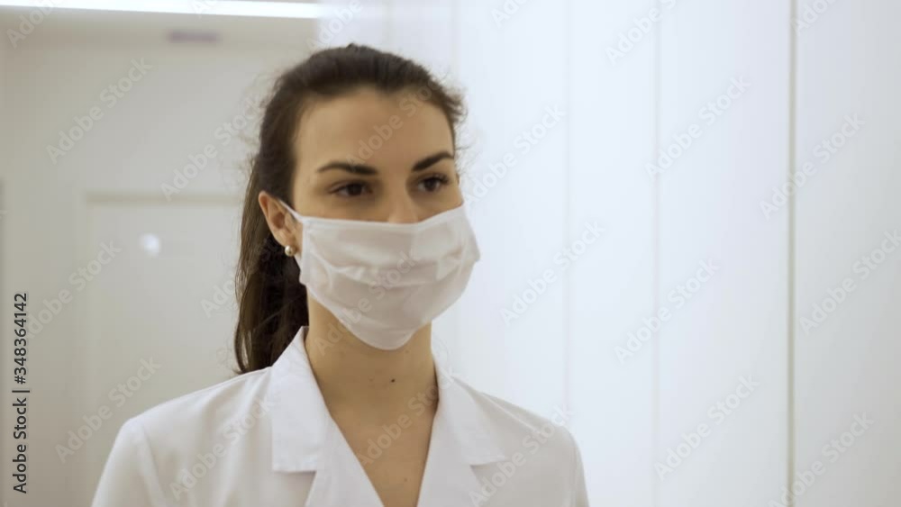 A masked female doctor walks down a corridor in the green zone of a modern clinic and reads medical records during a quarantine pandemic A masked female doctor walks down a corridor in the green zone of a modern clinic and reads medical records during a quarantine pandemic