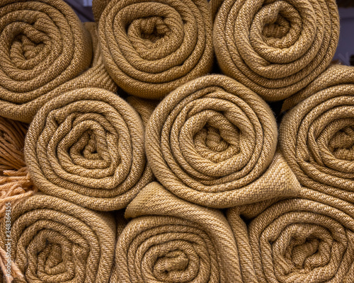 A pile of knitted beige plaid folded into a roll. Several handmade woolen texture blanket in stock.