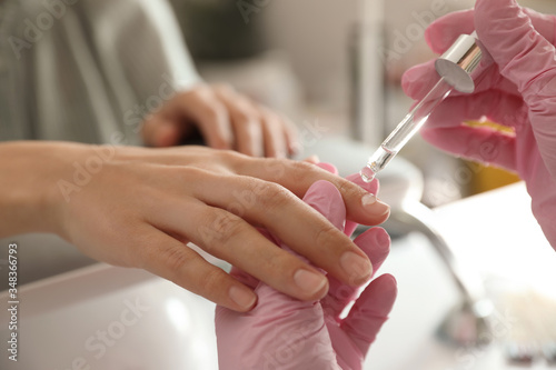Professional manicurist pouring oil on client's nails in beauty salon, closeup